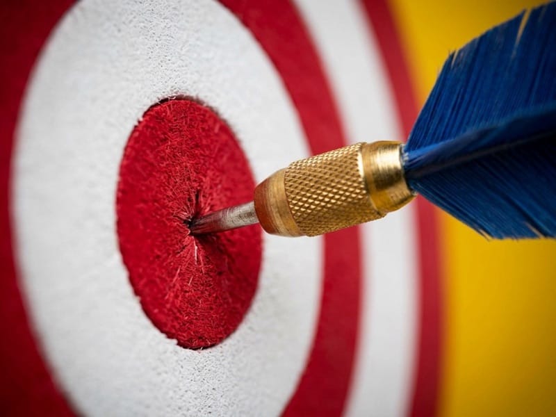 Blue-feathered dart landing in the red bullseye of a target