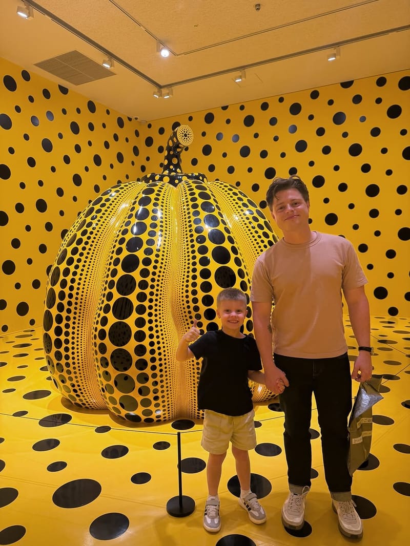 Father and son posing in front of a giant yellow polka-dot pumpkin sculpture by Yayoi Kusama