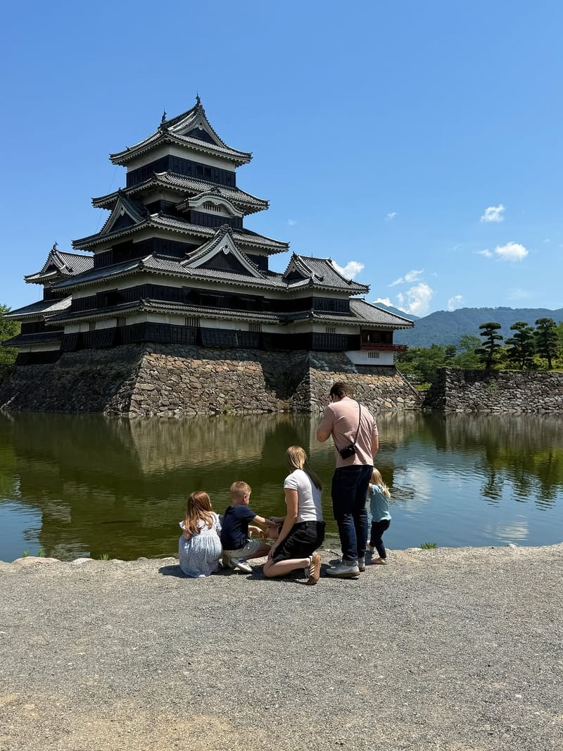 Family of five sitting by the moat looking at Matsumoto Castle under a blue sky