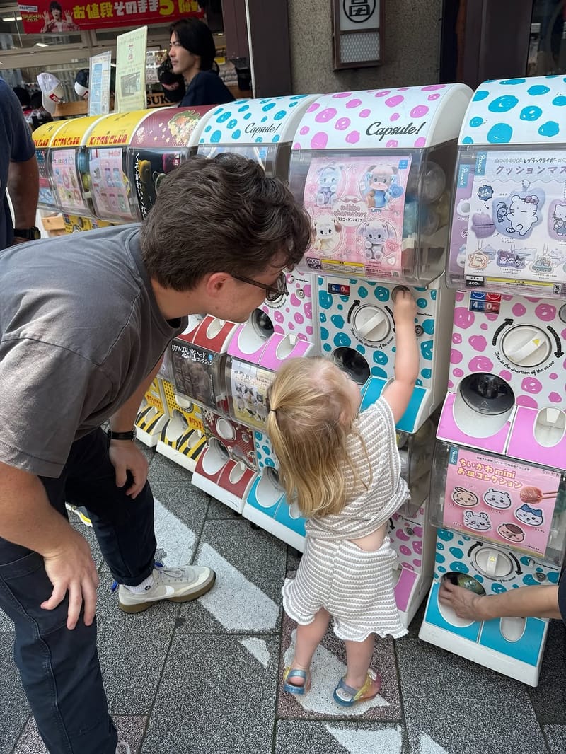 Father and toddler trying Japanese capsule toy machines on a busy street