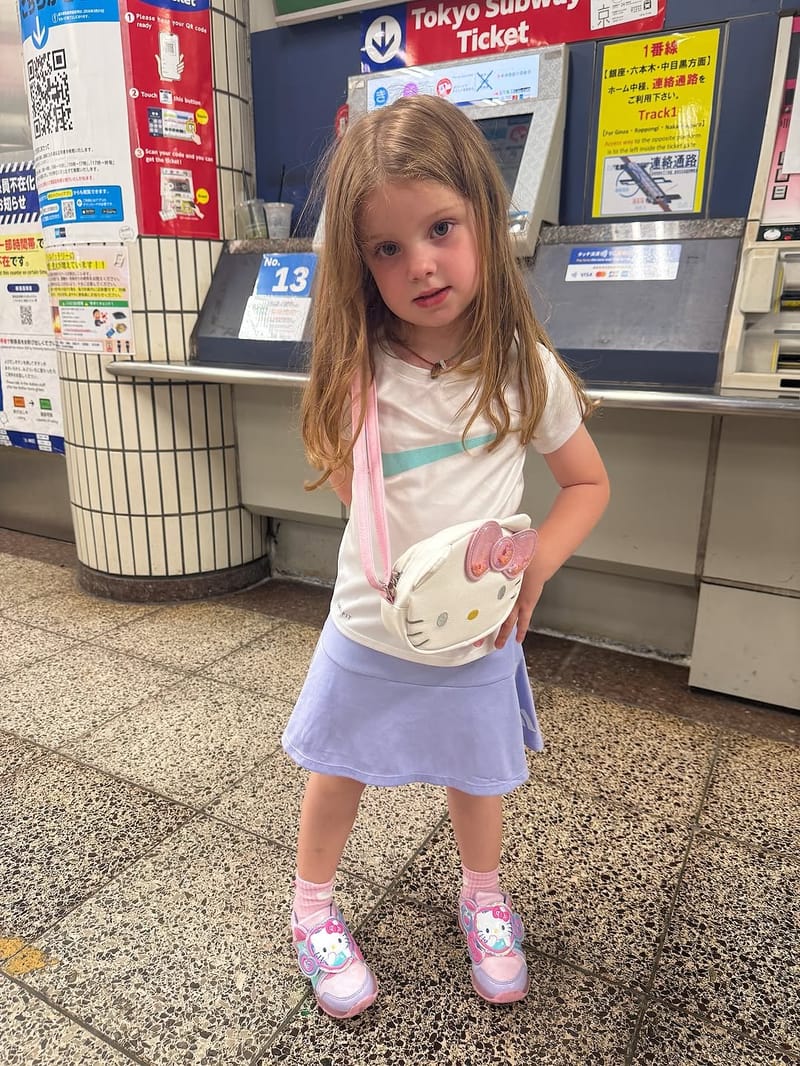 Young girl with long hair posing at a Tokyo Subway ticket counter with a Hello Kitty bag