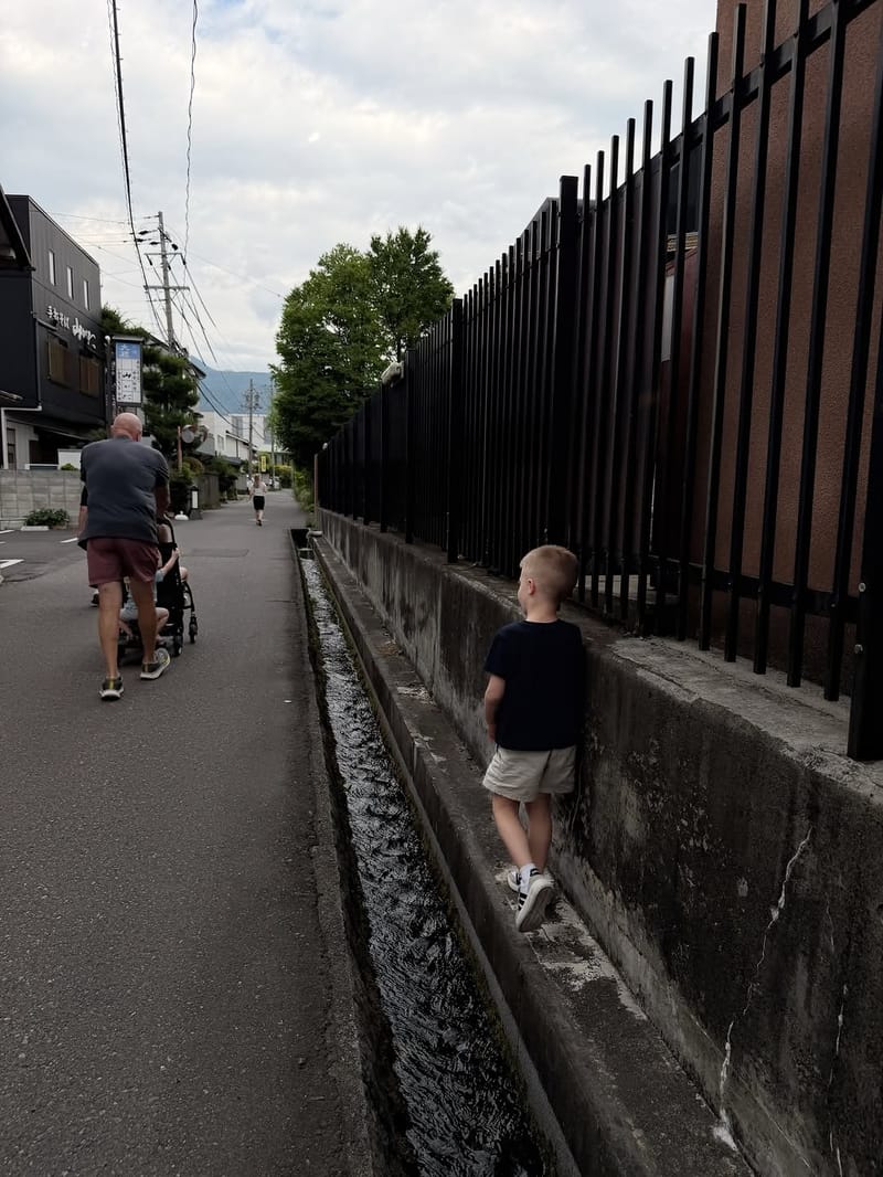 Young boy balancing on a concrete ledge beside a water drainage channel on a quiet Japanese street