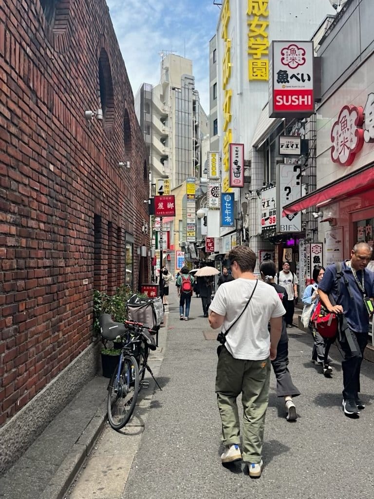 Man walking through a narrow Tokyo alley lined with sushi signs and brick buildings