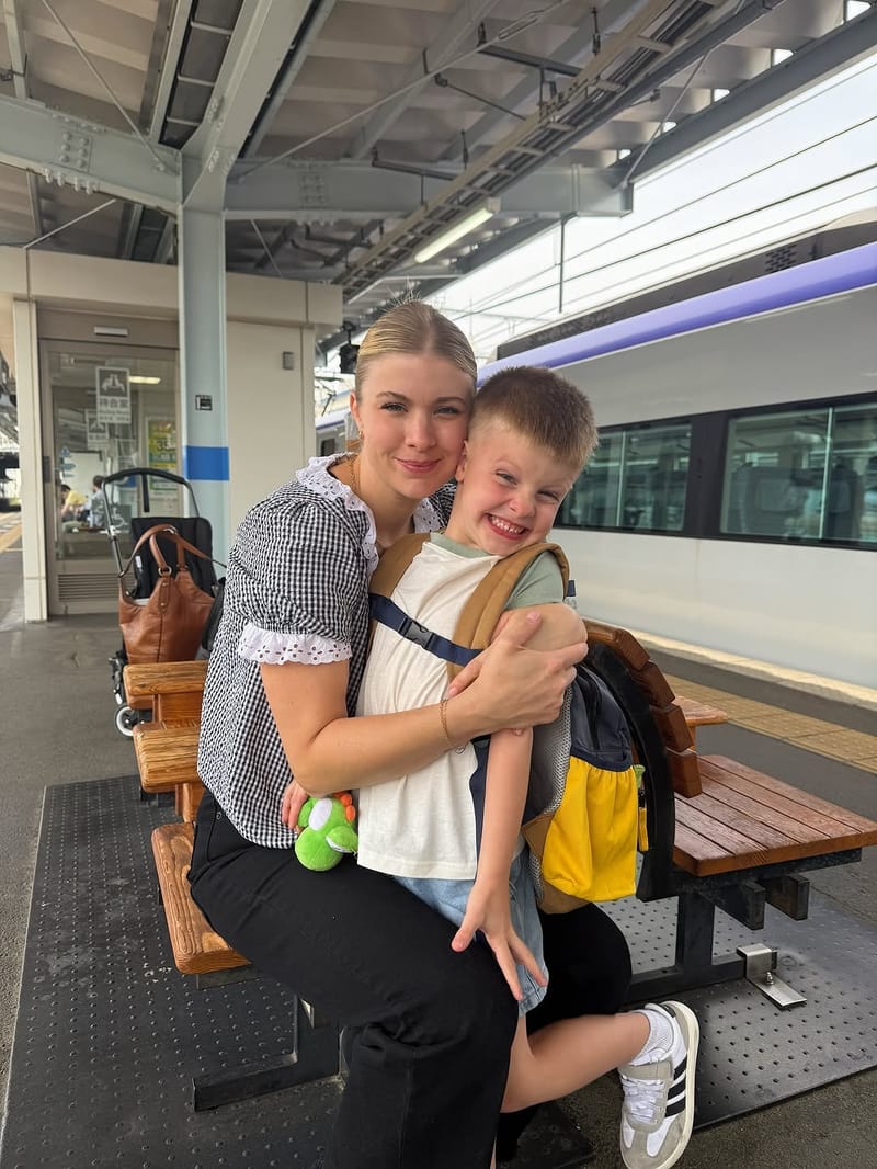 Mother hugging her smiling son on a train platform bench with a bullet train in the background